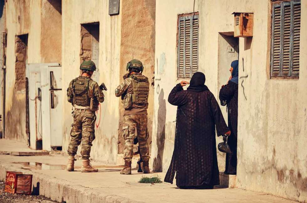 Zwei Soldaten, daneben zwei verschleiere syrische Frauen im Hauseingang